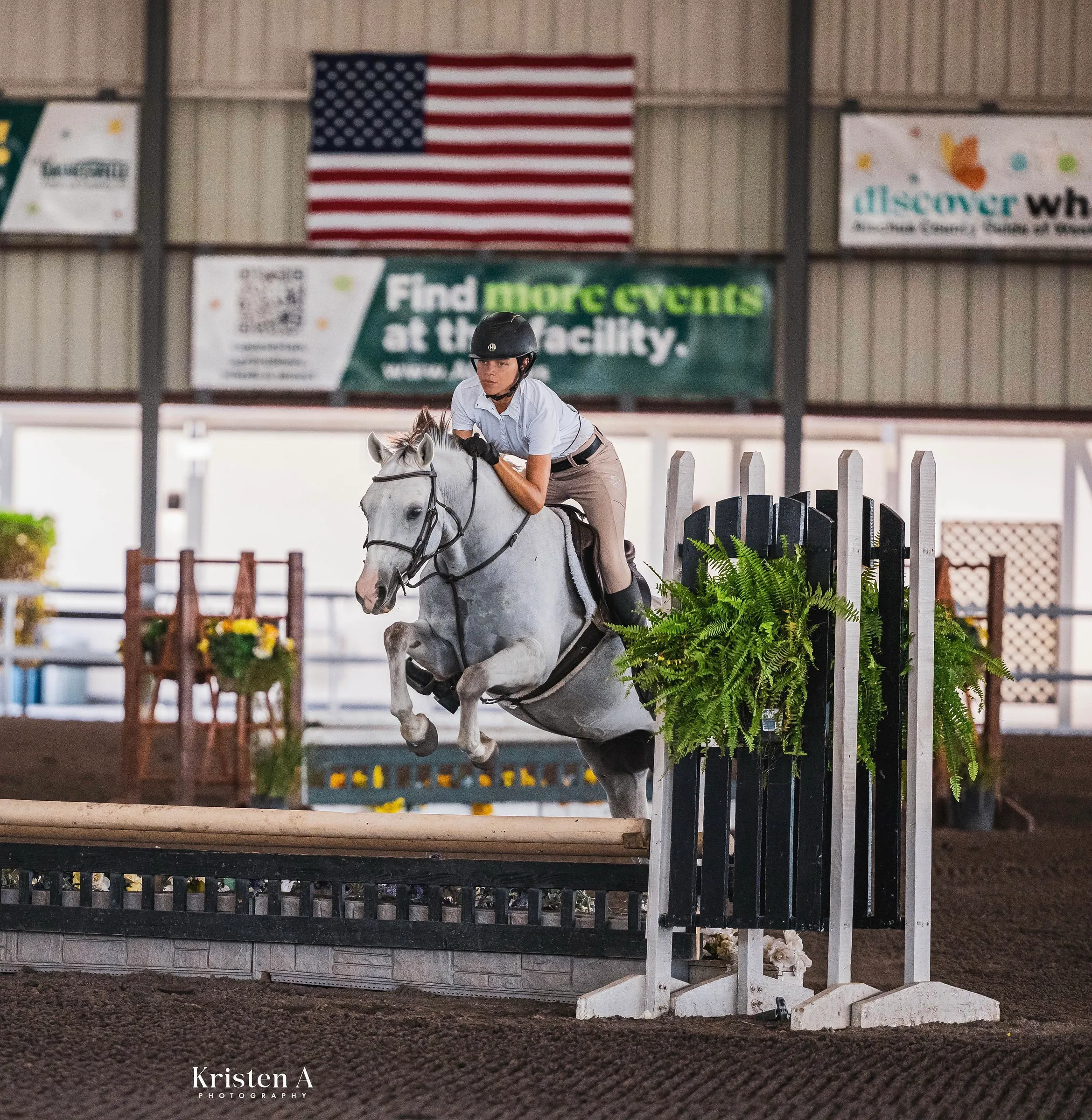 A grey horse and rider clearing a jump in a show ring